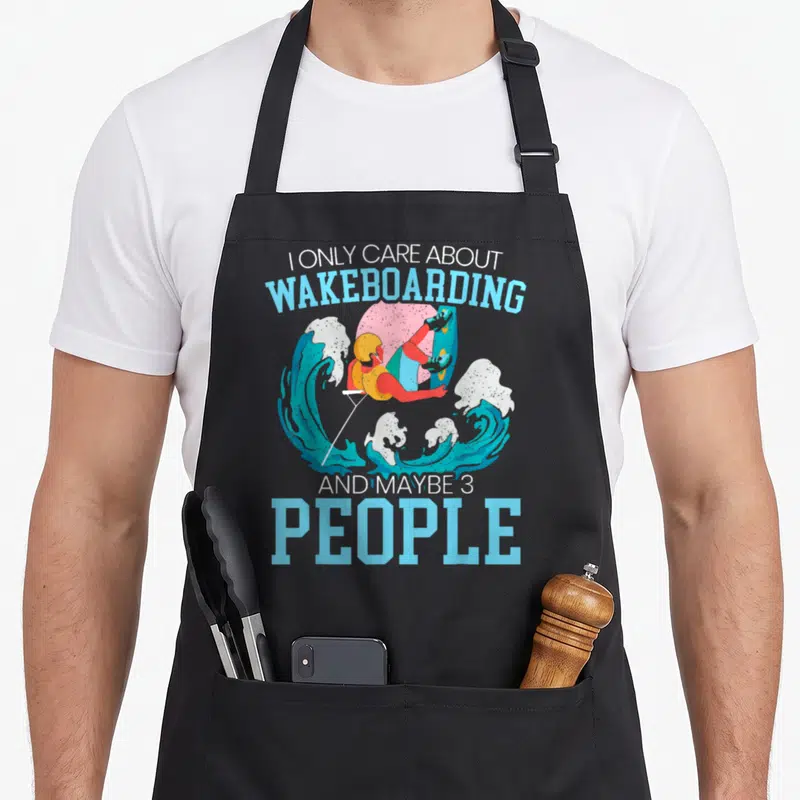 Tablier de cuisine noir avec illustration colorée d'un wakeboarder effectuant un saut au-dessus d'une grande vague bleue.