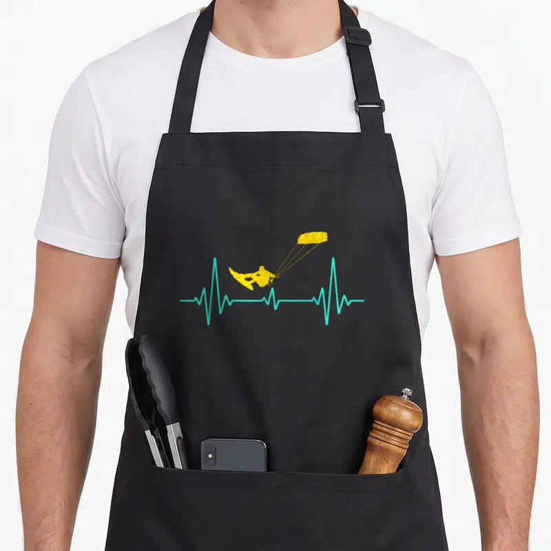 Tablier de cuisine noir avec un kiteboard jaune sur une ligne de rythme cardiaque turquoise.