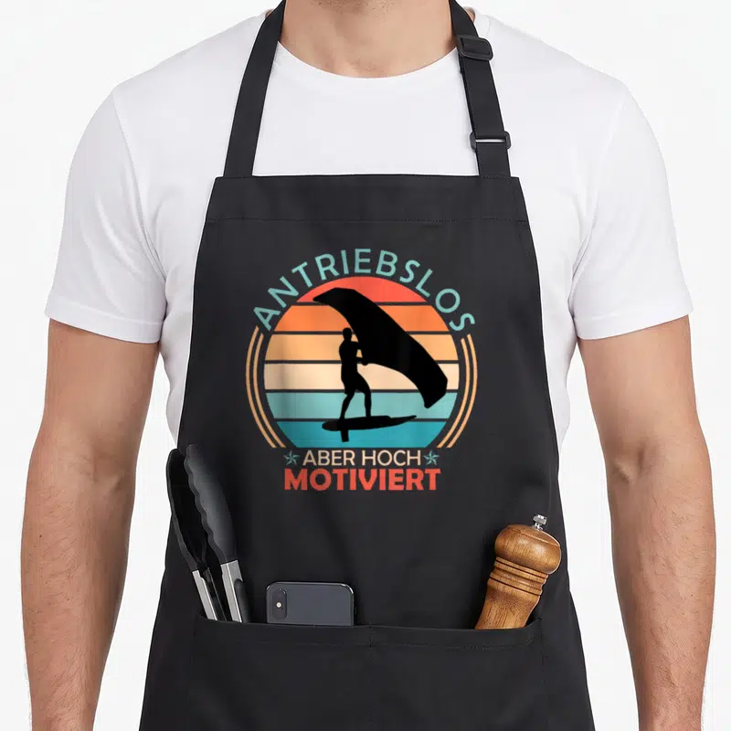 Tablier de cuisine noir avec silhouette wing foiler et texte Antriebslos Aber Hoch Motiviert sur fond de soleil vintage.