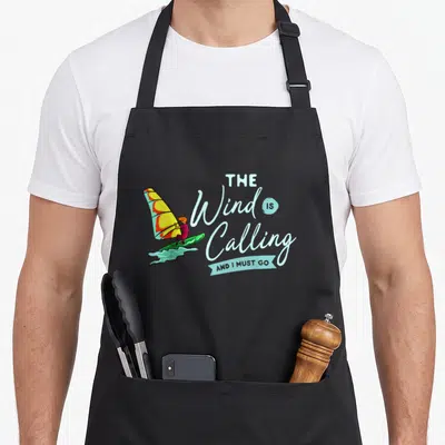 Tablier de cuisine noir avec illustration d'un windsurfer et texte The Wind Is Calling And I Must Go en bleu clair.