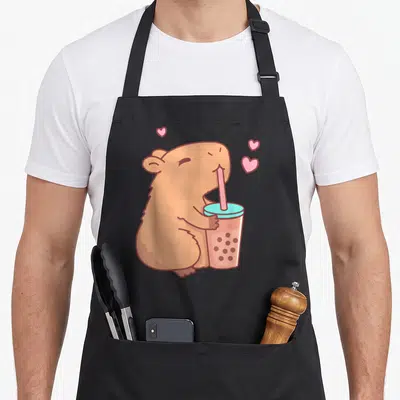 Tablier de cuisine noir avec un capybara marron buvant une boisson rose à la paille.