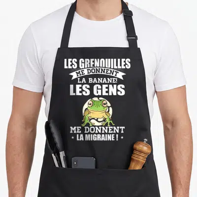 Tablier de cuisine noir avec une illustration de grenouille verte et un message humoristique en blanc sur le devant.
