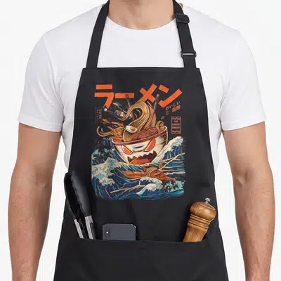 Tablier de cuisine noir avec illustration d'un bol de ramen aux yeux menaçants sur des vagues bleues et des caractères japonais orange.