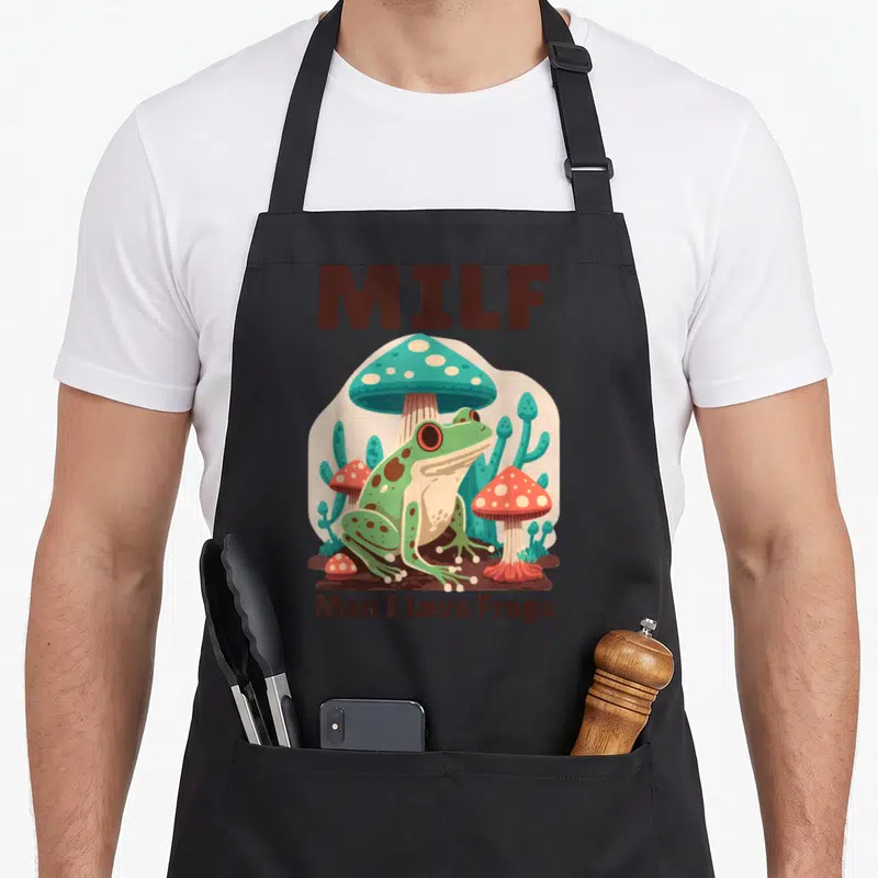 Tablier de cuisine noir avec illustration d'une grenouille verte sous un grand champignon turquoise et les mots MILF Man I Love Frogs.