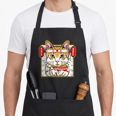 Tablier de cuisine noir avec illustration d'un chat tigré mangeant du ramen entre deux lanternes rouges.