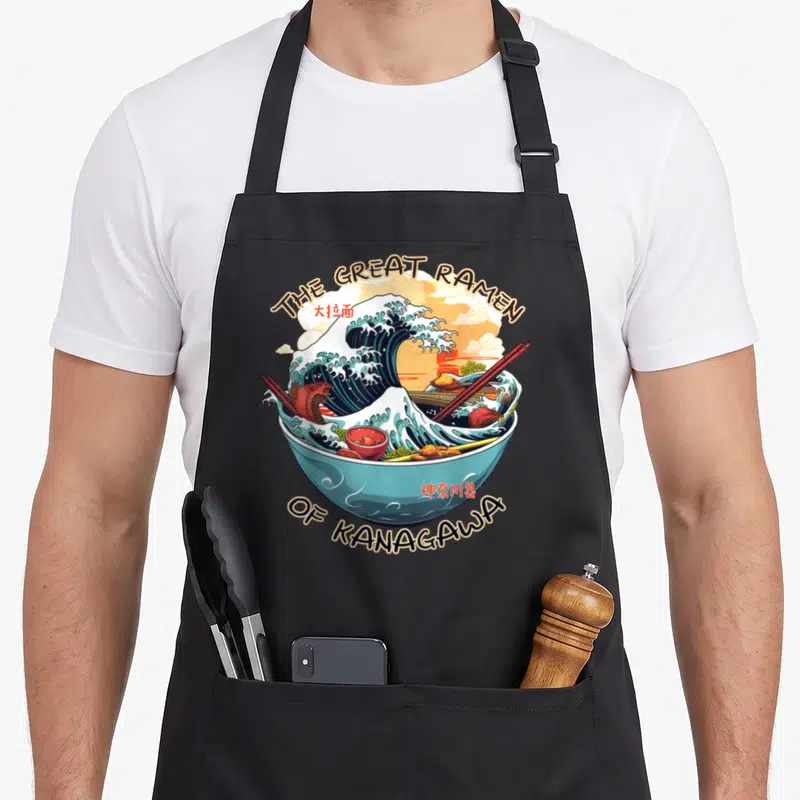 Tablier de cuisine noir avec illustration d'un bol de ramen transformé en grande vague stylisée et chopsticks rouges.
