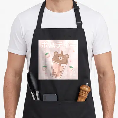 Tablier de cuisine noir avec illustration d'un thé aux perles en forme d'ours, de fraises et de texte japonais sur fond rose.