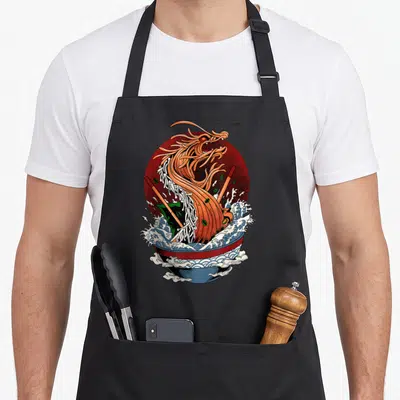Tablier de cuisine noir avec un dragon orange sortant d'un bol de ramen sur fond de soleil rouge.