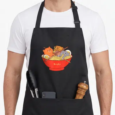 Tablier de cuisine noir avec illustration de trois chats mangeant des nouilles ramen dans un bol rouge avec des baguettes.