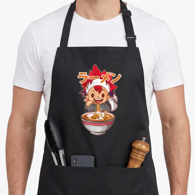 Tablier de cuisine noir avec un personnage aux cheveux rouges mangeant du ramen dans un bol décoré.