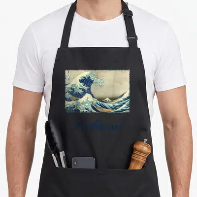 Tablier de cuisine noir avec La grande vague devant Kanagawa et le mot Hokusai en calligraphie bleue.