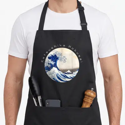 Tablier de cuisine noir avec une illustration circulaire de La Grande Vague et le nom Katsushika Hokusai en arc de cercle.