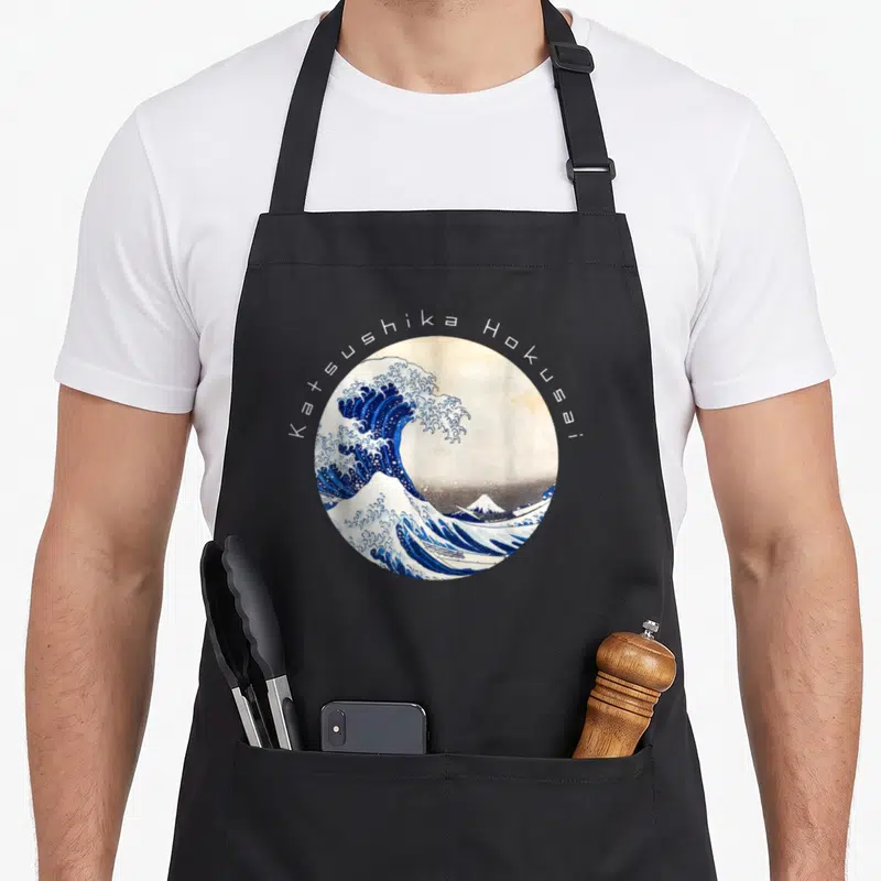 Tablier de cuisine noir avec une illustration circulaire de La Grande Vague et le nom Katsushika Hokusai en arc de cercle.