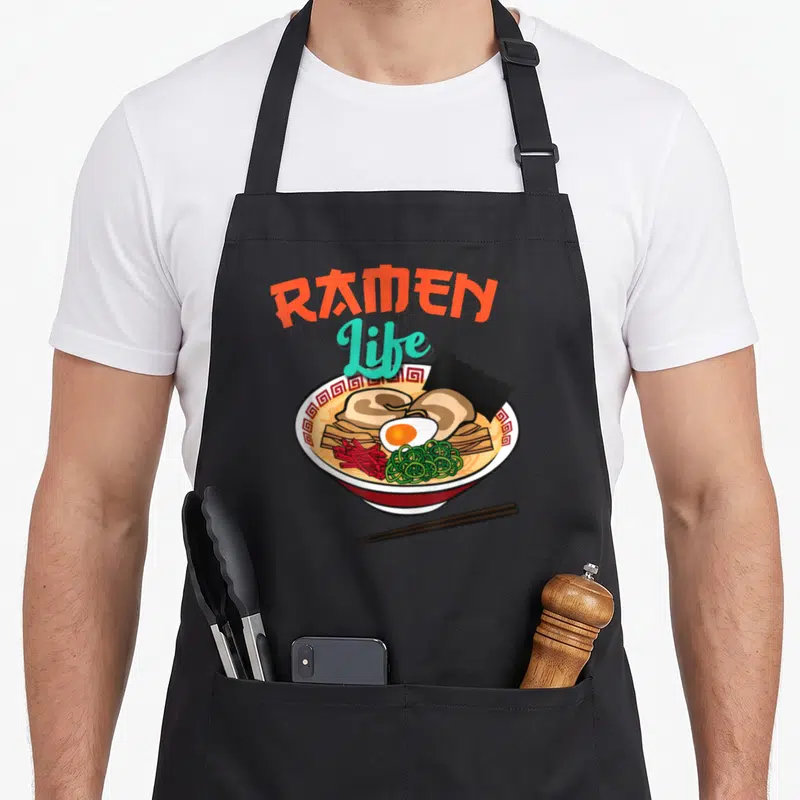 Tablier de cuisine noir avec illustration colorée d'un bol de ramen et du texte Ramen Life au-dessus.