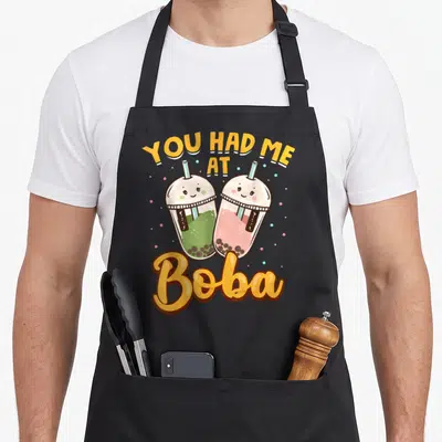 Tablier de cuisine noir avec deux verres de boba kawaii souriants et l'inscription You Had Me At Boba en lettres orange.