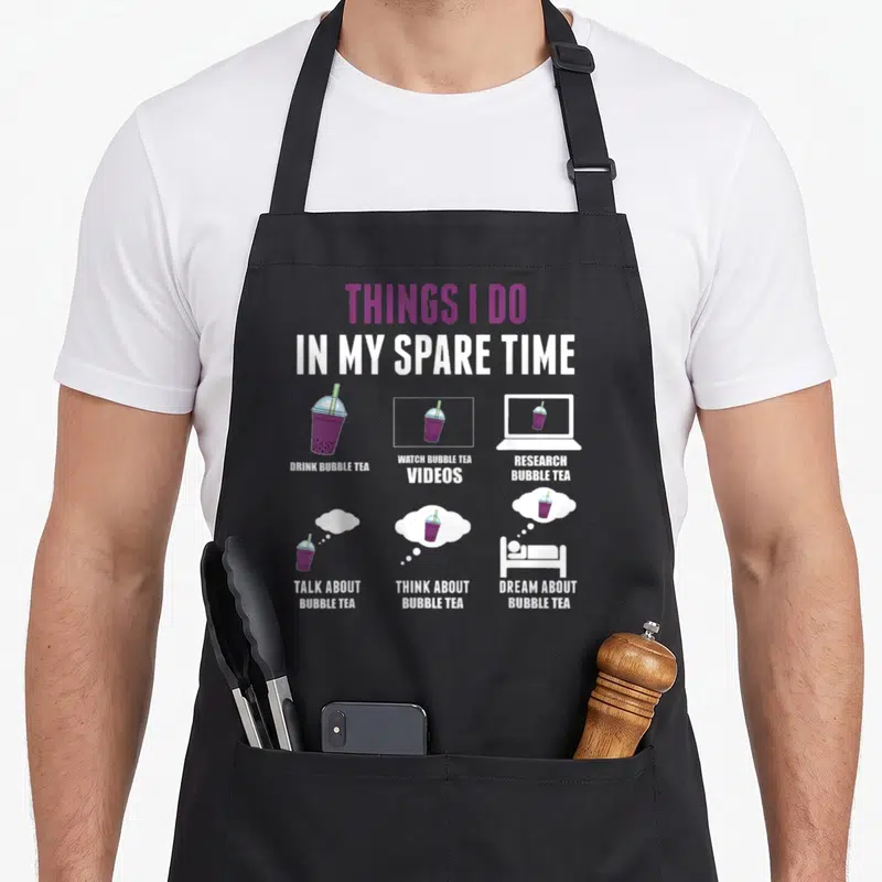 Tablier de cuisine noir avec illustration colorée représentant des tasses de bubble tea et un ordinateur portable.