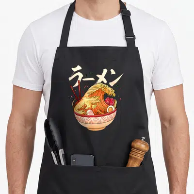 Tablier de cuisine noir avec une illustration colorée représentant une vague de ramen sortant d'un bol décoré de motifs ondulés.