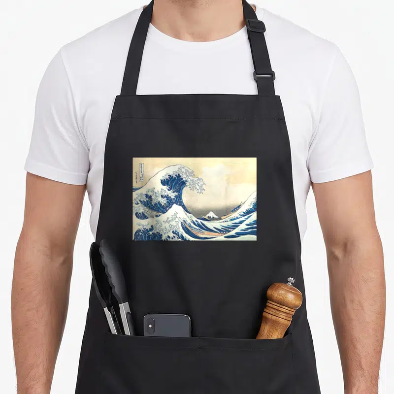 Tablier de cuisine noir avec La grande vague au large de Kanagawa imprimé en bleu et blanc.