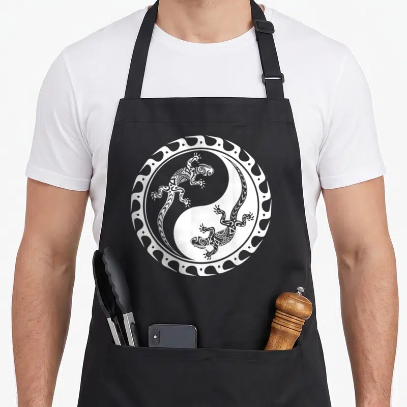 Tablier de cuisine noir avec illustration blanche d'une salamandre maori dans un cercle yin yang tribal polynésien.