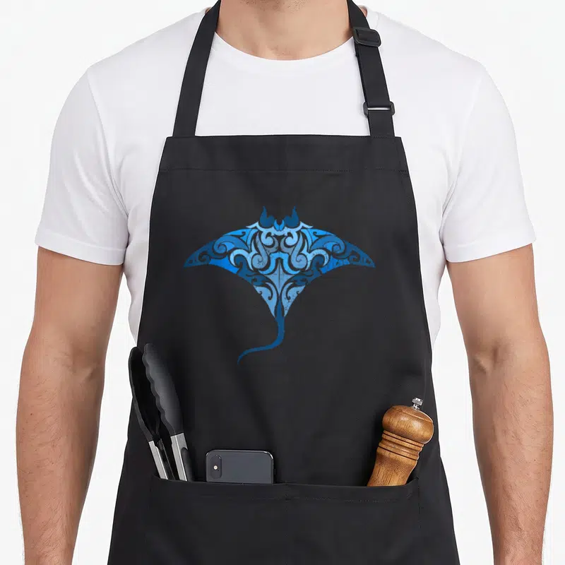 Tablier de cuisine noir avec illustration bleue d'une raie manta aux motifs tribaux et ornementaux inspirés du style maori.