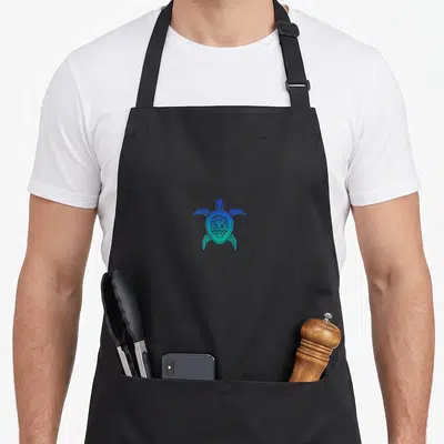 Tablier de cuisine noir avec une tortue maori tribale aux couleurs bleu et vert turquoise.