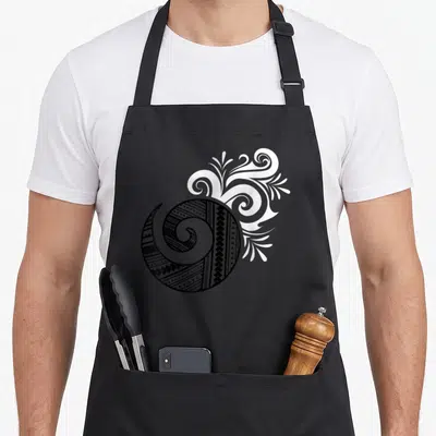 Tablier de cuisine noir avec motif tatouage Maori tribal en spirale et éléments végétaux stylisés en blanc.