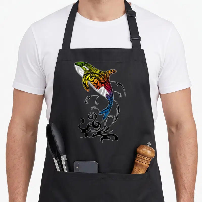 Tablier de cuisine noir avec illustration d'orque sautante aux motifs tribaux colorés et vifs.