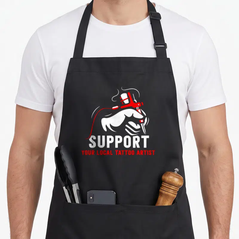 Tablier de cuisine noir avec illustration main tenant une machine à tatouer rouge et texte blancSupport Your Local Tattoo Artist.