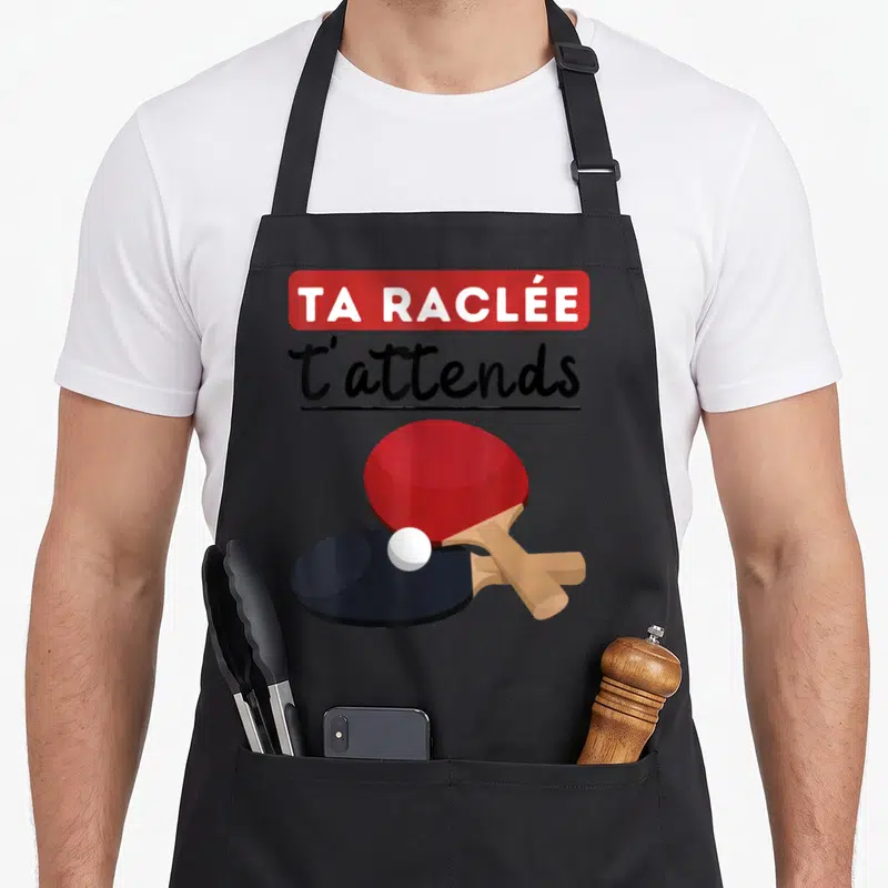 Tablier de cuisine noir avec une raquette rouge, une raquette noire et une balle de ping-pong sous le texte Ta raclée t'attends