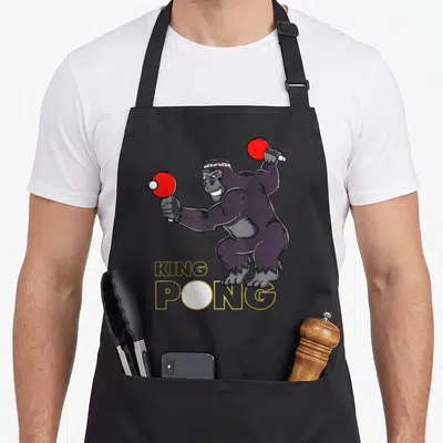 Tablier de cuisine noir avec illustration d'un gorille jouant au ping-pong et le texte King Pong en jaune.