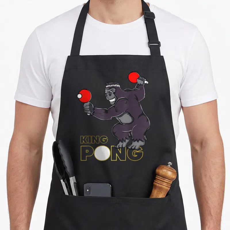 Tablier de cuisine noir avec illustration d'un gorille jouant au ping-pong et le texte King Pong en jaune.