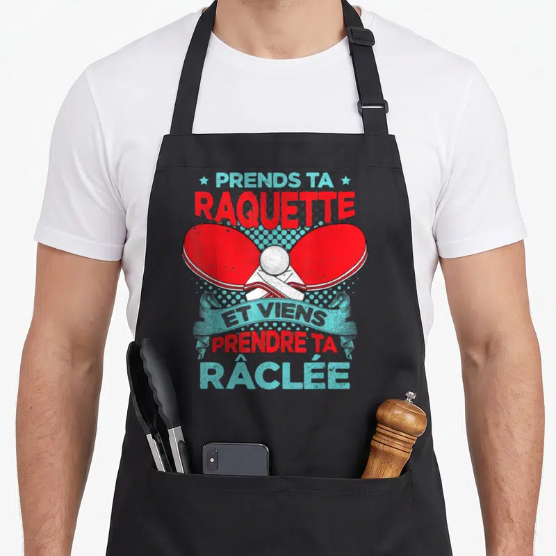 Tablier de cuisine noir avec deux raquettes de ping-pong rouges croisées et un ballon blanc au centre.
