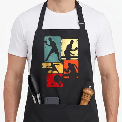 Tablier de cuisine noir avec silhouettes de joueurs de ping-pong dans des rectangles bleu, jaune et orange aux effets usés.