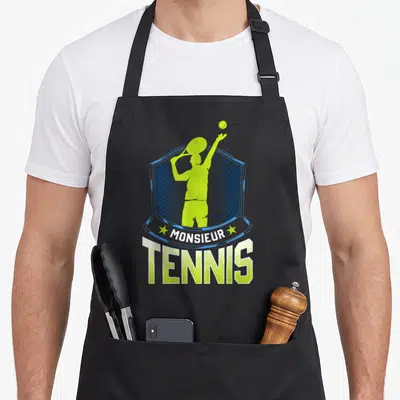 Tablier de cuisine noir avec un joueur de tennis vert lime et le texte Monsieur Tennis sur fond d'écusson bleu.