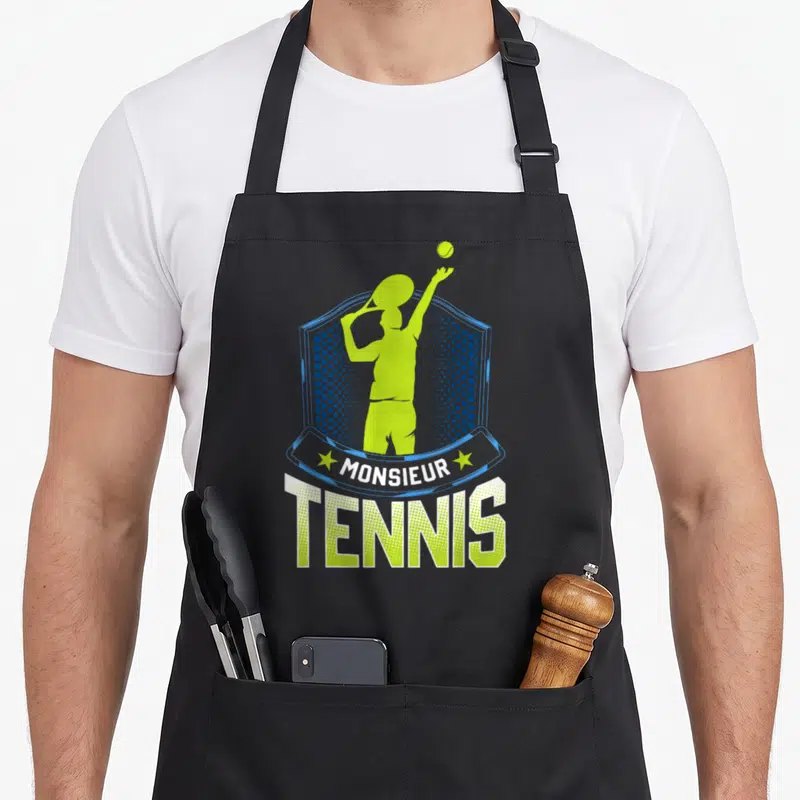 Tablier de cuisine noir avec un joueur de tennis vert lime et le texte Monsieur Tennis sur fond d'écusson bleu.