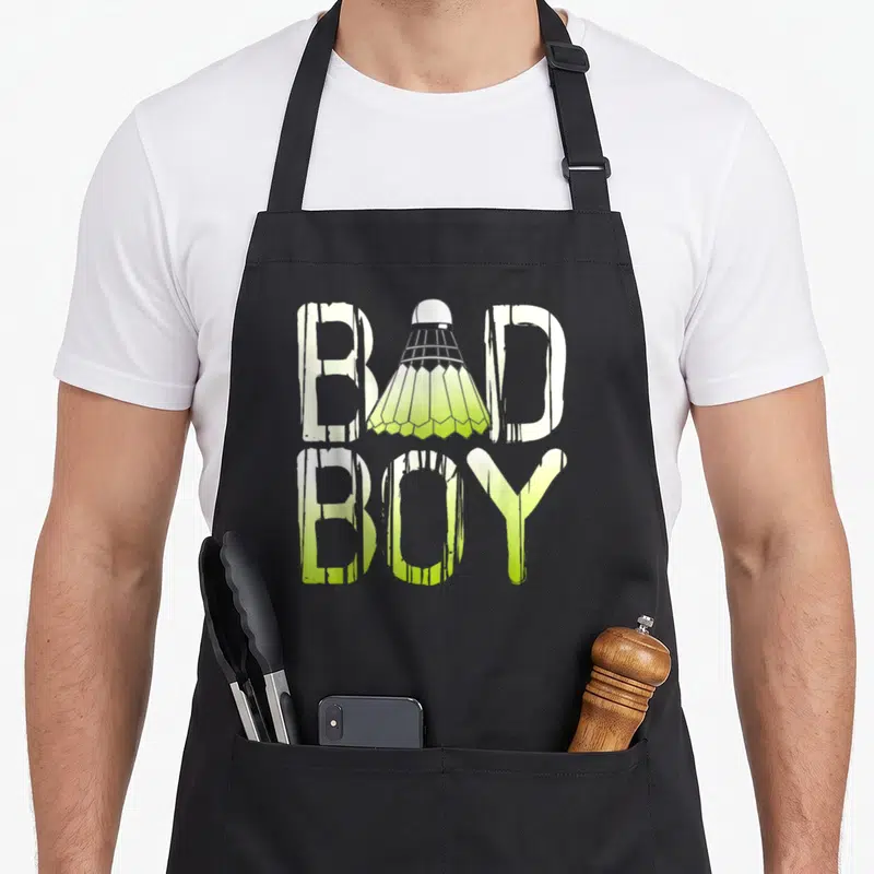 Tablier de cuisine noir avec l'inscription Bad Badminton Boy où un volant remplace la lettre A du mot bad.