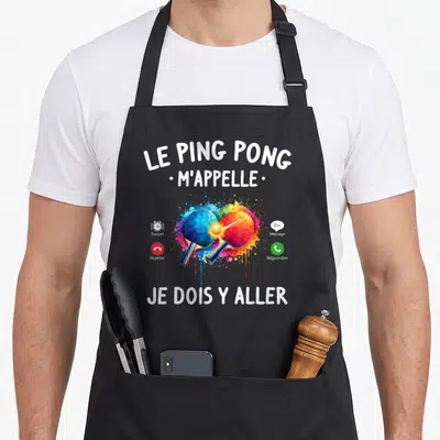 Tablier de cuisine noir avec deux raquettes de ping-pong colorées et texte blanc sur fond gris uni.