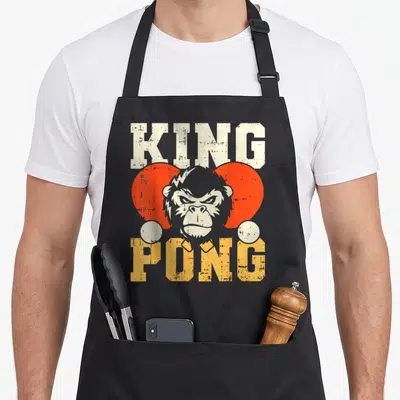 Tablier de cuisine noir avec illustration d'un gorille et le texte KING PONG en lettres délavées orange et crème.