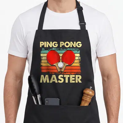 Tablier de cuisine noir avec deux raquettes de ping pong croisées et le texte Ping Pong Master en style vintage.