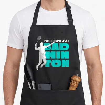 Tablier de cuisine noir avec une silhouette blanche de joueur de badminton et un texte turquoise en gros caractères.