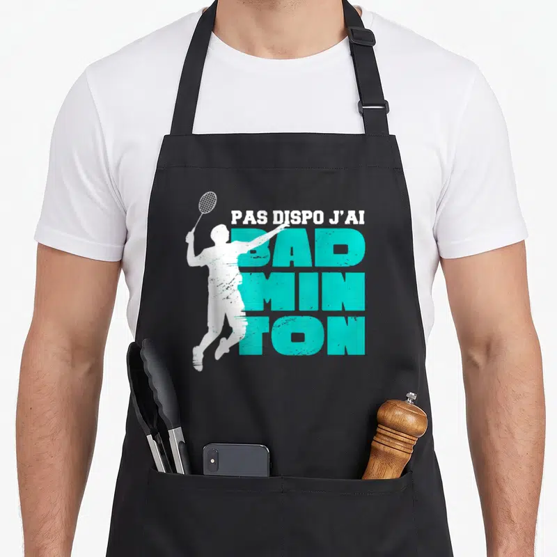 Tablier de cuisine noir avec une silhouette blanche de joueur de badminton et un texte turquoise en gros caractères.