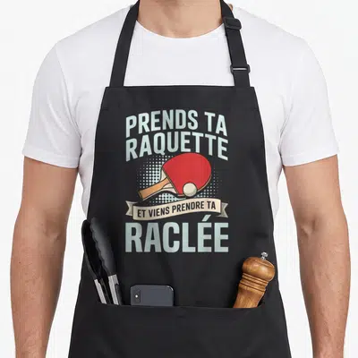 Tablier de cuisine noir avec une raquette de ping-pong rouge et un ballon blanc sur fond de points gris clair.
