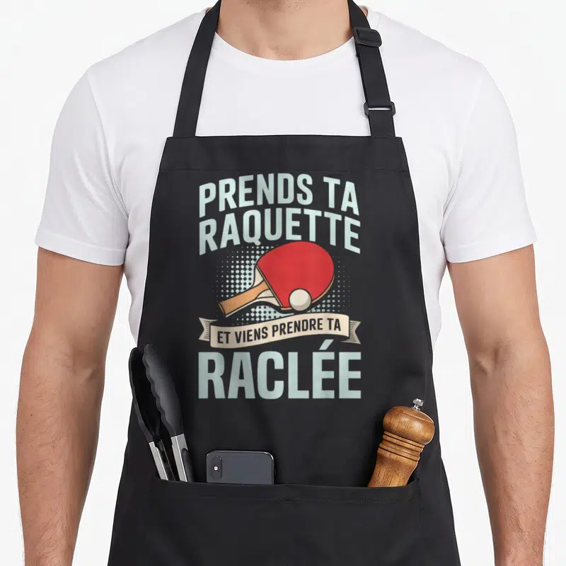 Tablier de cuisine noir avec une raquette de ping-pong rouge et un ballon blanc sur fond de points gris clair.