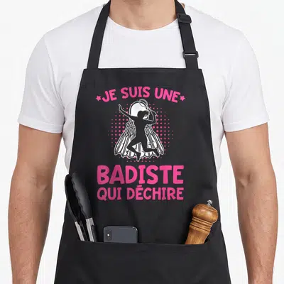 Tablier de cuisine noir avec illustration rose et blanche d'une badine sautant au-dessus d'un volants et du texte Je suis une badiste qui déchire.