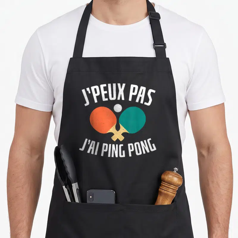 Tablier de cuisine noir avec inscription Je peux pas j'ai ping pong et deux raies de tennis de table croisées orange et verte.