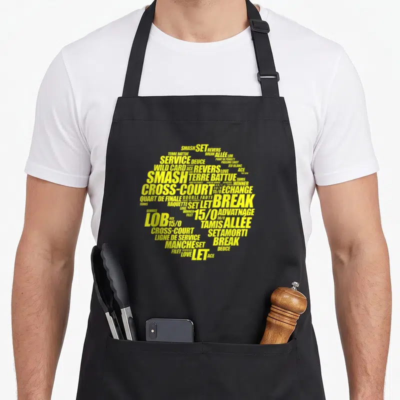 Tablier de cuisine noir avec un motif typographique jaune représentant une balle de tennis composée de termes de jeu.