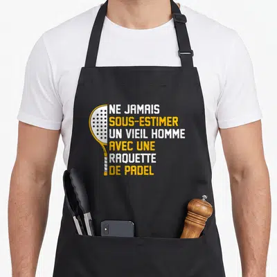 Tablier de cuisine noir avec une raquette de padel jaune et le texte Ne jamais sous-estimer un vieil homme avec une raquette de padel