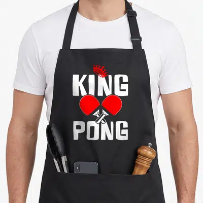 Tablier de cuisine noir avec inscription King Pong, couronne rouge et deux raquettes de ping-pong croisées en rouge et blanc.