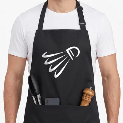 Tablier de cuisine noir avec illustration blanche d'un shuttle de badminton en mouvement dynamique sur fond uni.
