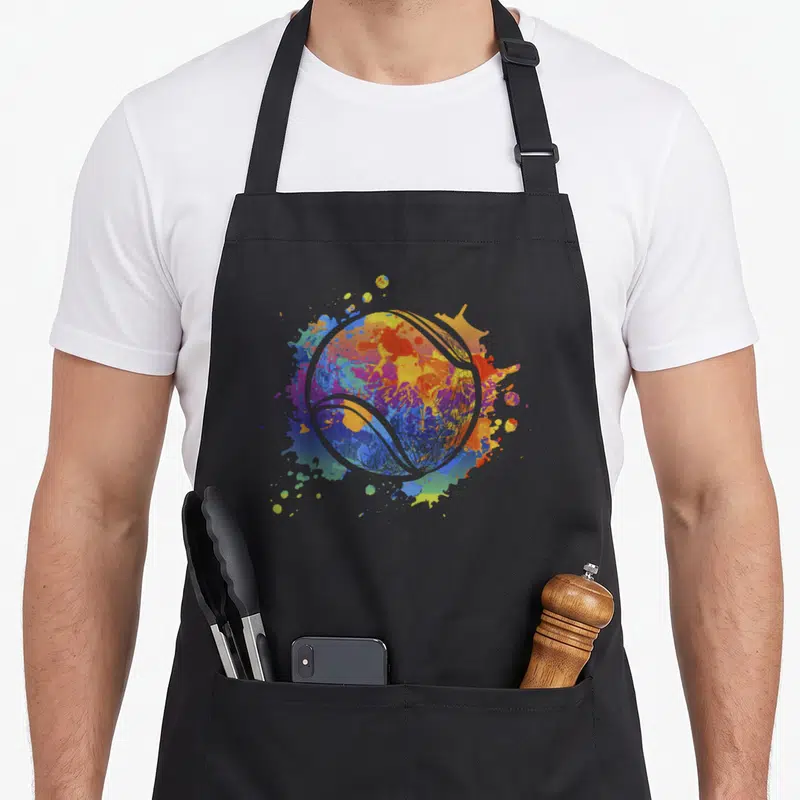 Tablier de cuisine noir avec une balle de tennis stylisée aux éclats de peinture colorée.